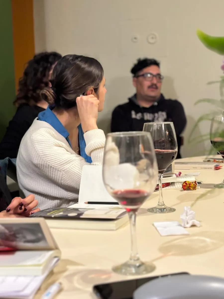 Participantes escuchando durante la charla, con el libro y una copa de vino sobre la mesa